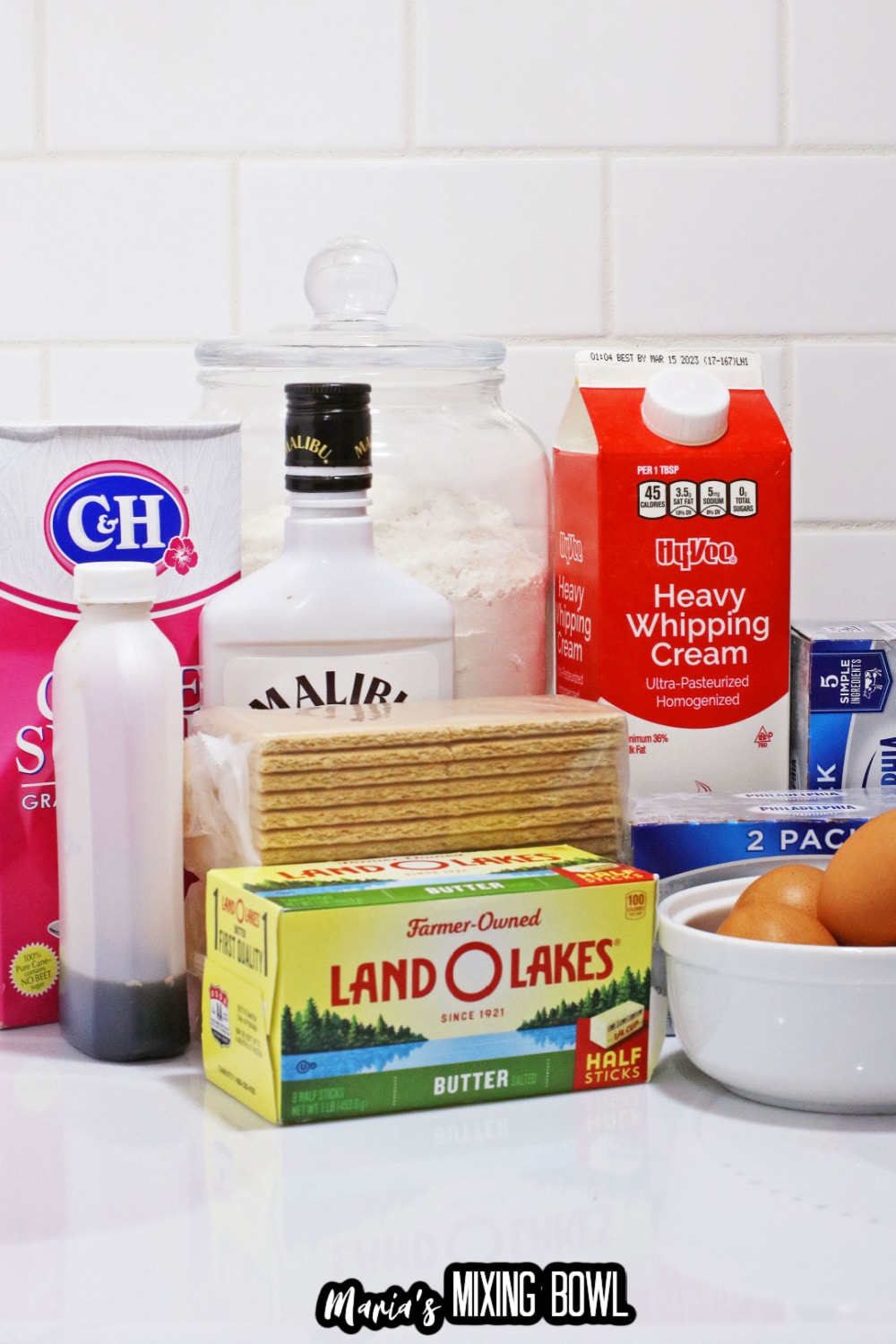 powdered sugar, vanilla, rum, whipping cream, cream cheese, graham crackers, butter and eggs on a white background