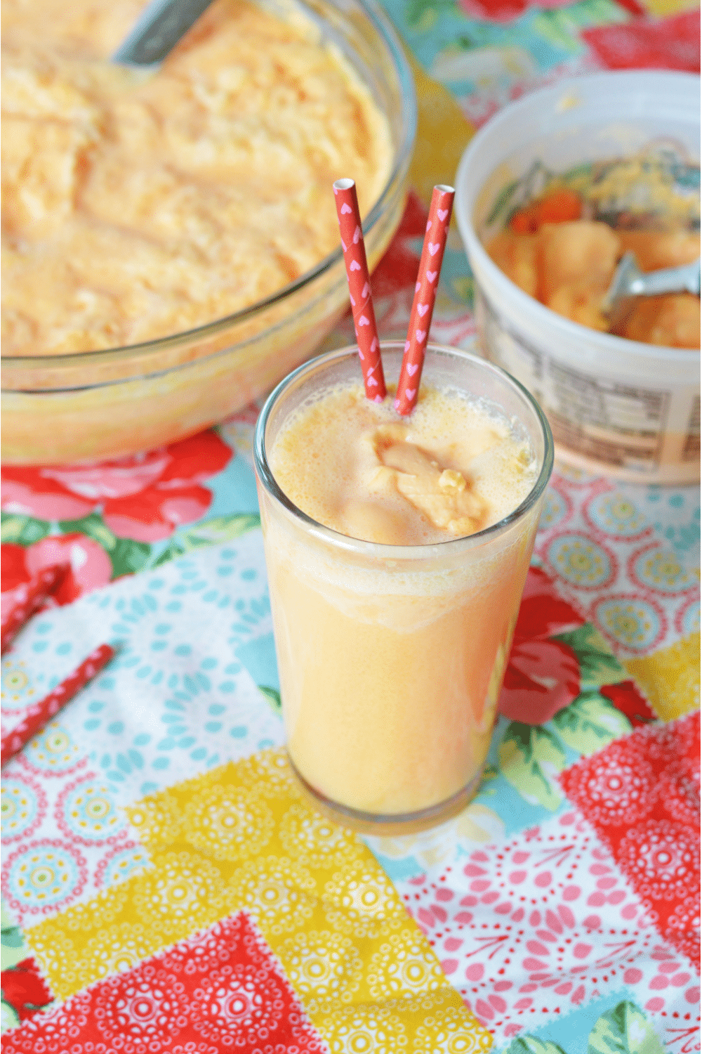 a glass of orange sherbet with two straws in it
