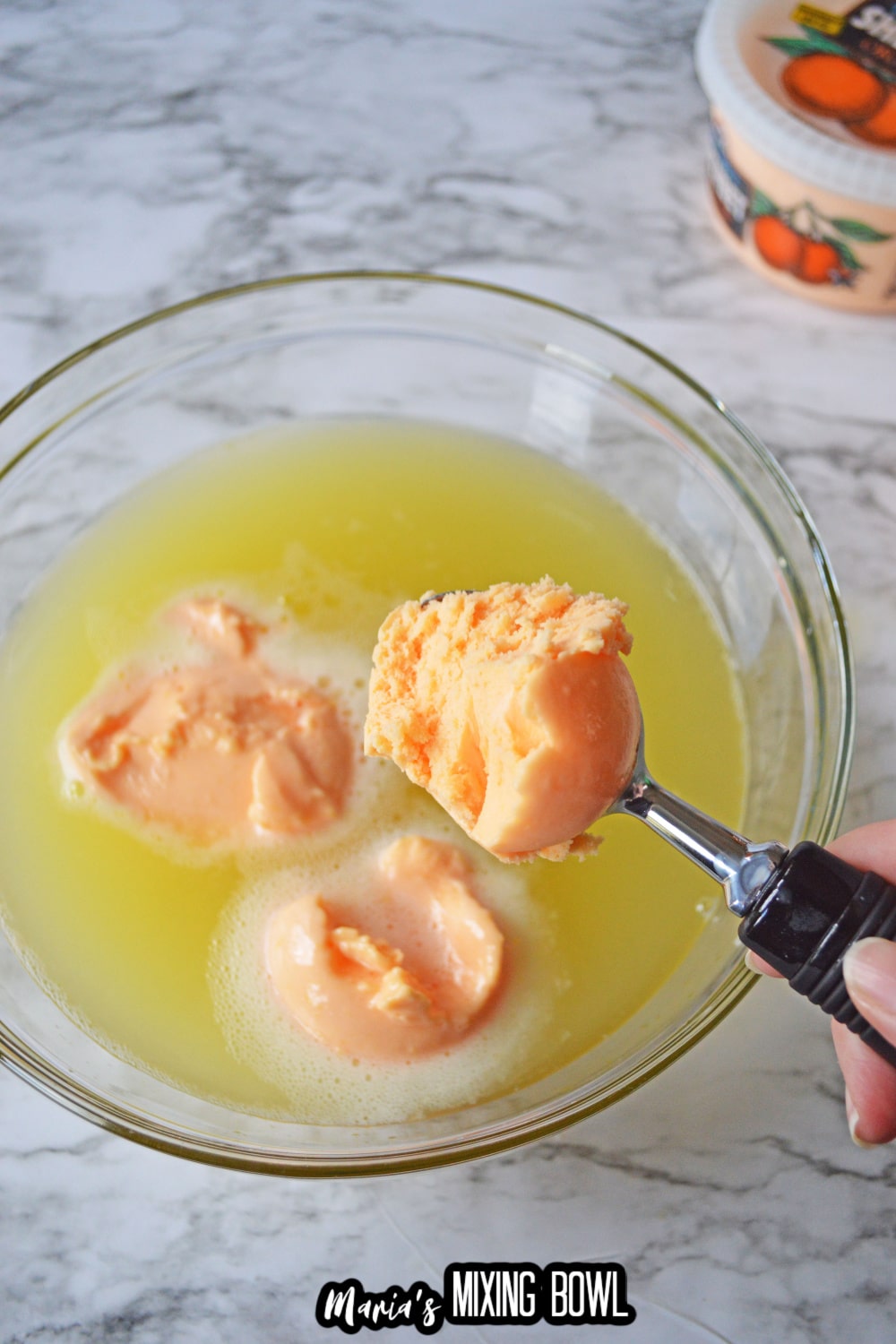 scoops of orange sherbet being added to a glass bowl