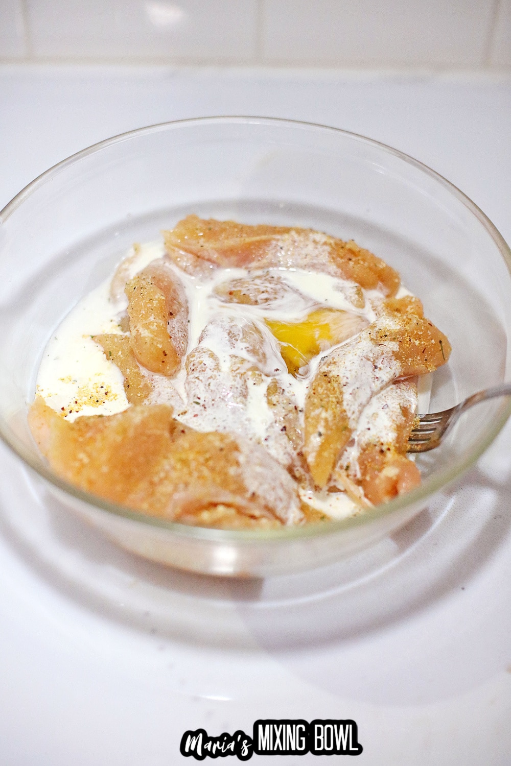 chicken tenderloins being coated in an egg wash in a small glass bowl