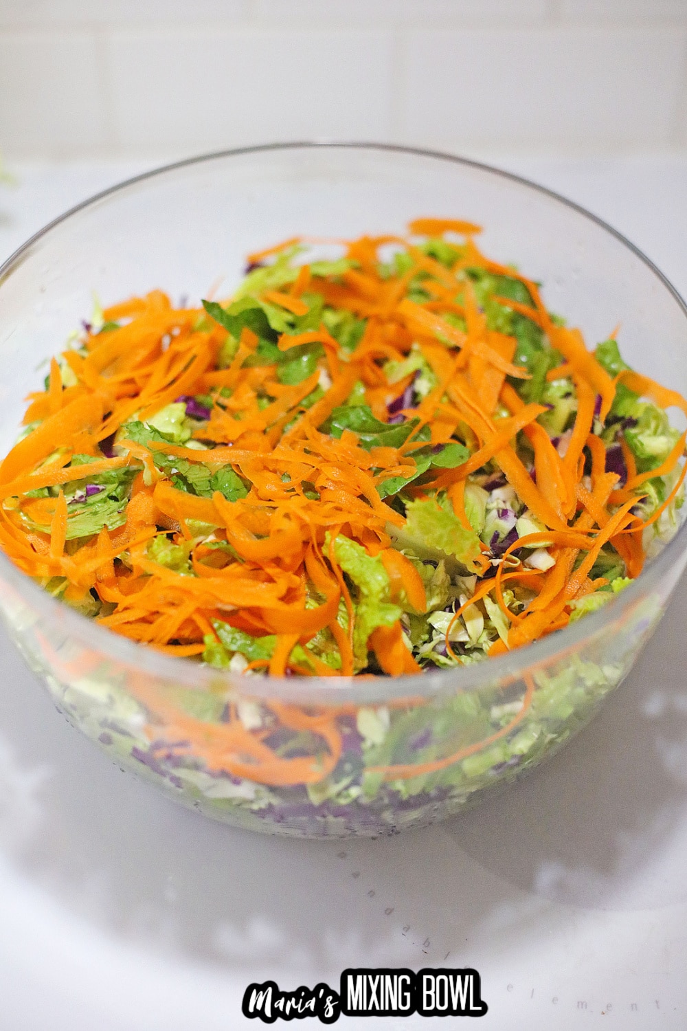 lettuce, and carrots being added to a large salad bowl