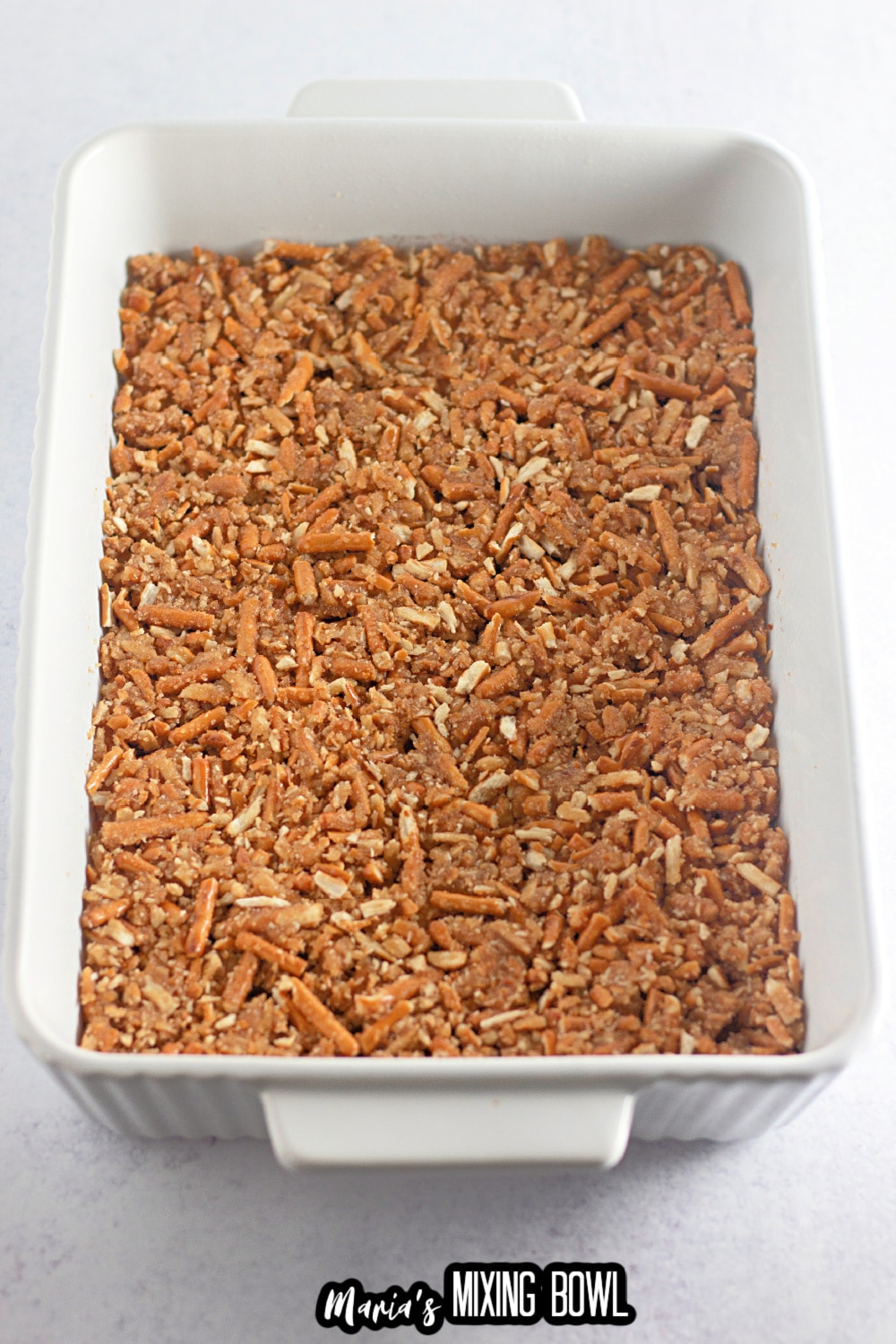pretzels being pressed into a white baking dish