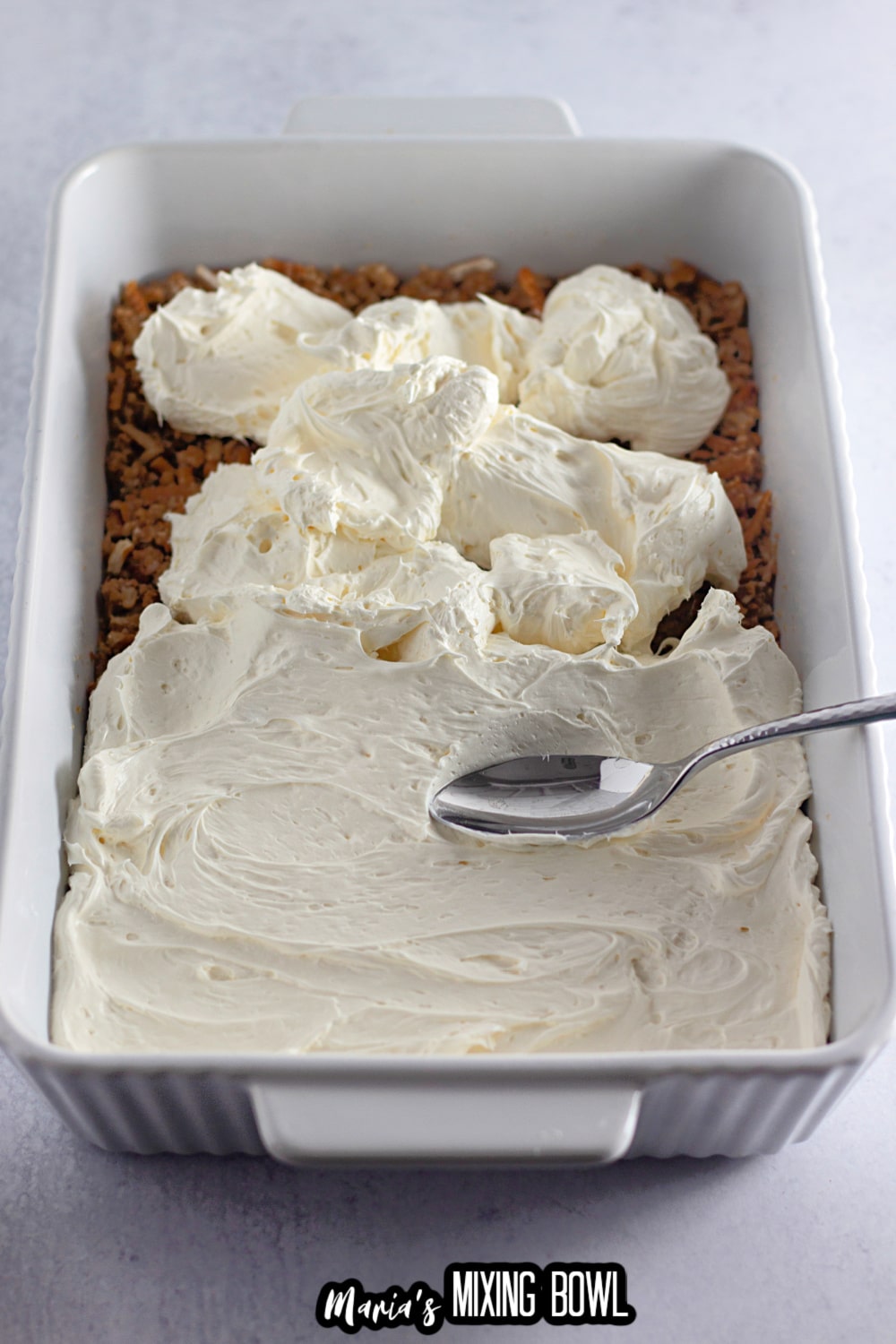 cream cheese layer being spread on top of a pretzel crust in a white baking dish