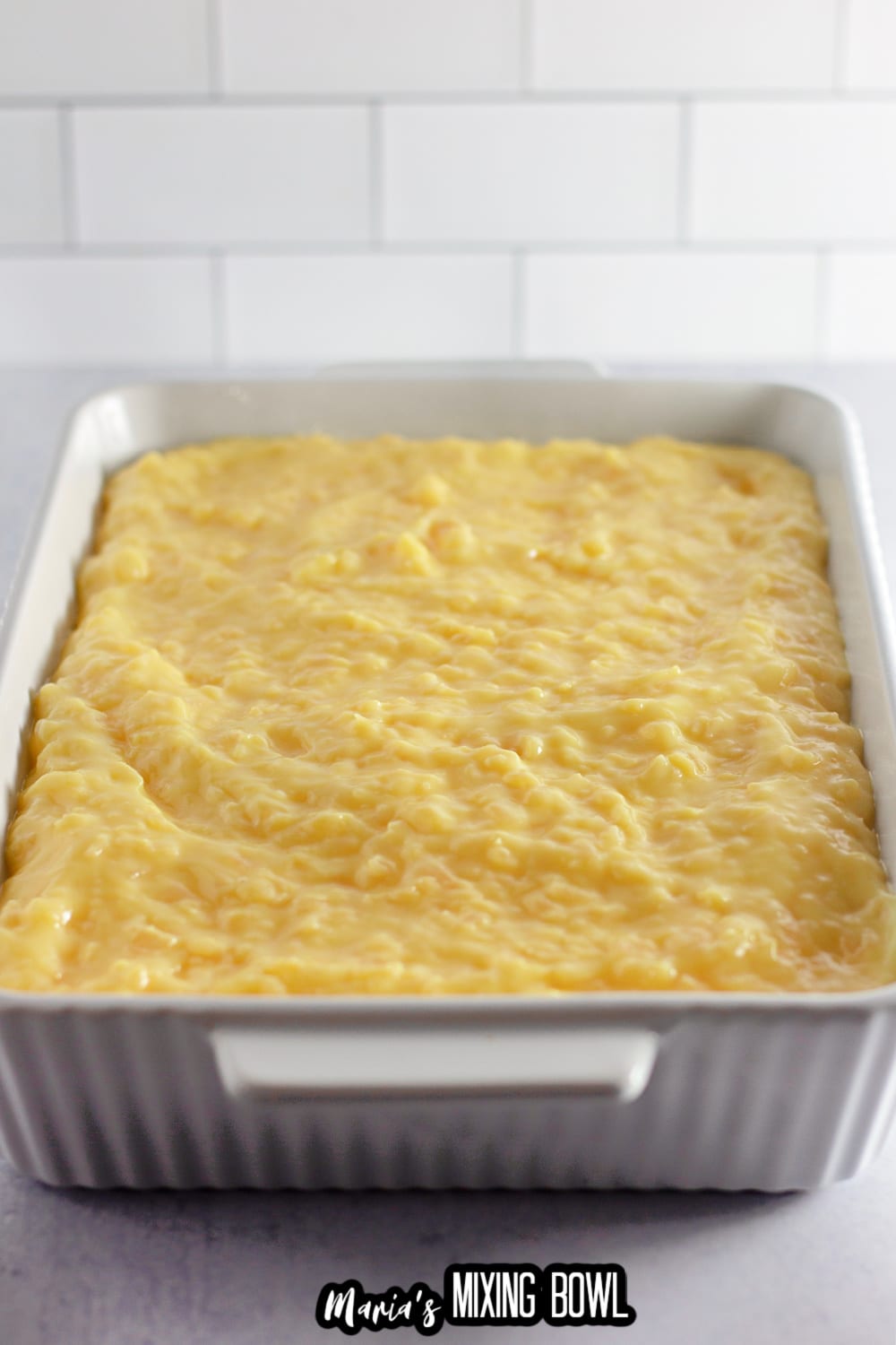 pineapple topping being added on top of a cream cheese layer in a white baking dish
