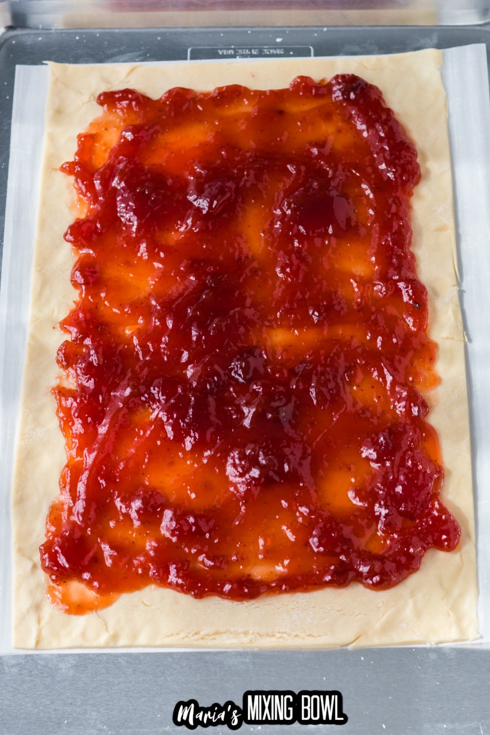 pie crust topped with strawberry jam on a parchment lined baking sheet