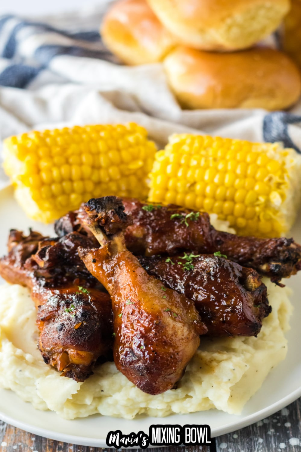 four chicken drumsticks on top of a bed of mashed potatoes with corn cobs in the background