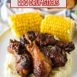 four chicken drumsticks on top of a bed of mashed potatoes with corn cobs in the background
