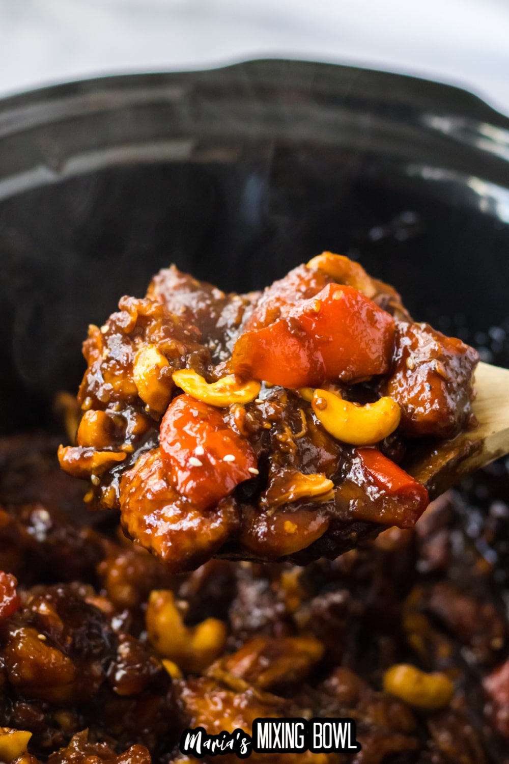 wooden spoon filled with cashew chicken held in the air above the slow cooker