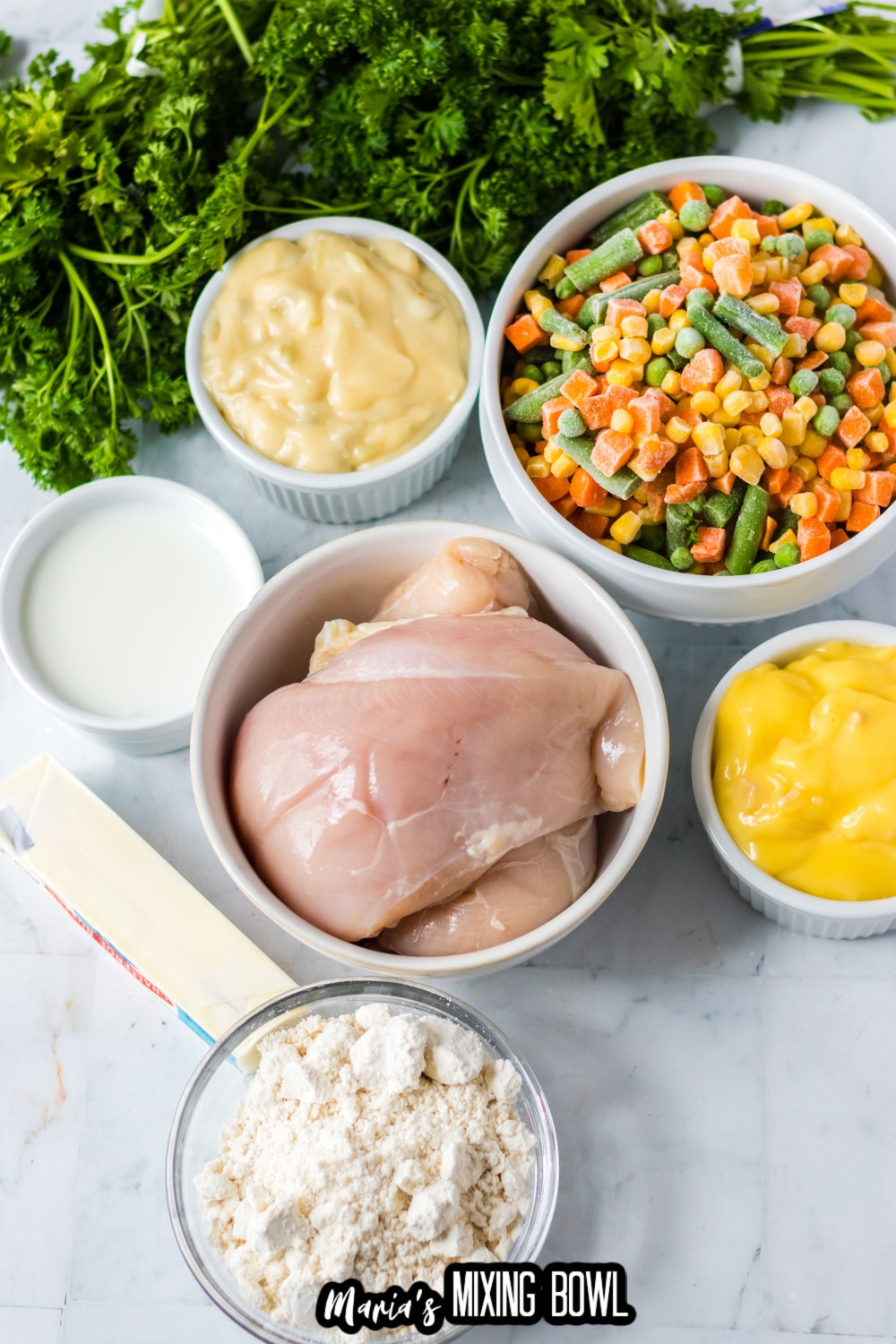 chicken breasts, cream of chicken soup, frozen mixed vegetables, milk, butter, and flour on a white marble background