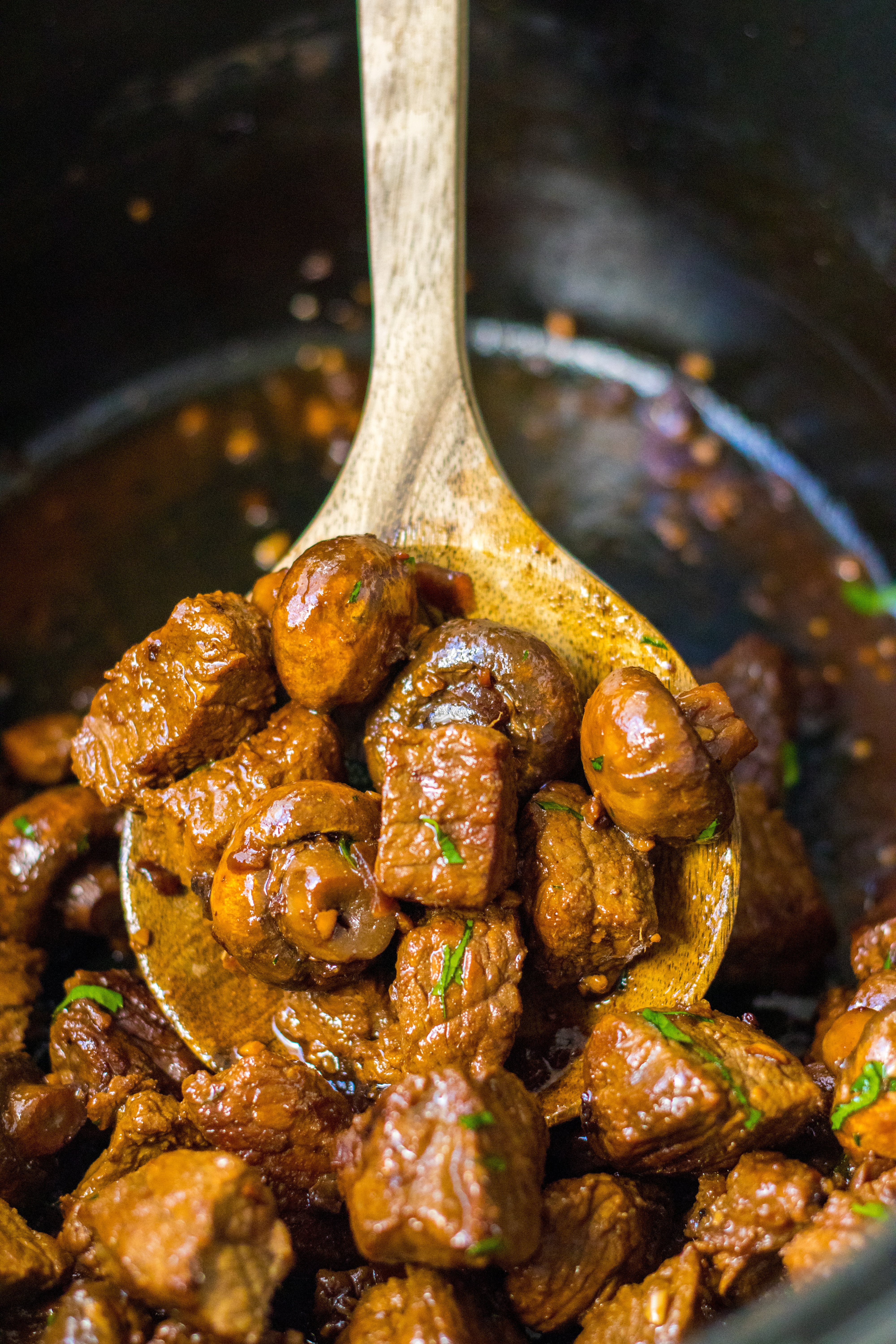 steak and mushrooms on a wooden spoon in a slow cooker