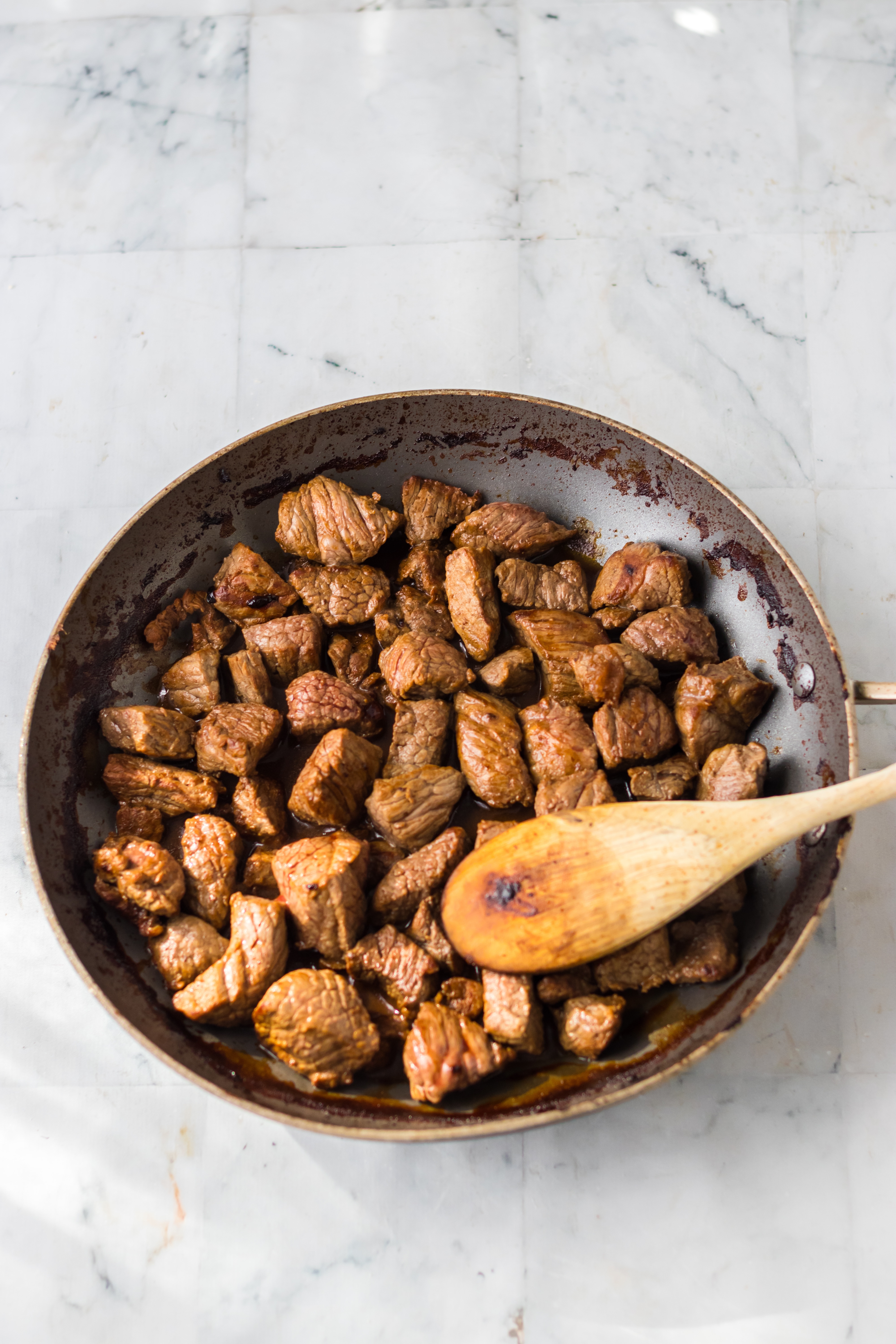 steak bites being seared in a skillet with a wooden spoon