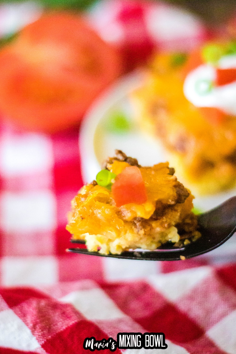 piece of tamale casserole on a fork held in the air above a table covered with a red and white check tablecloth