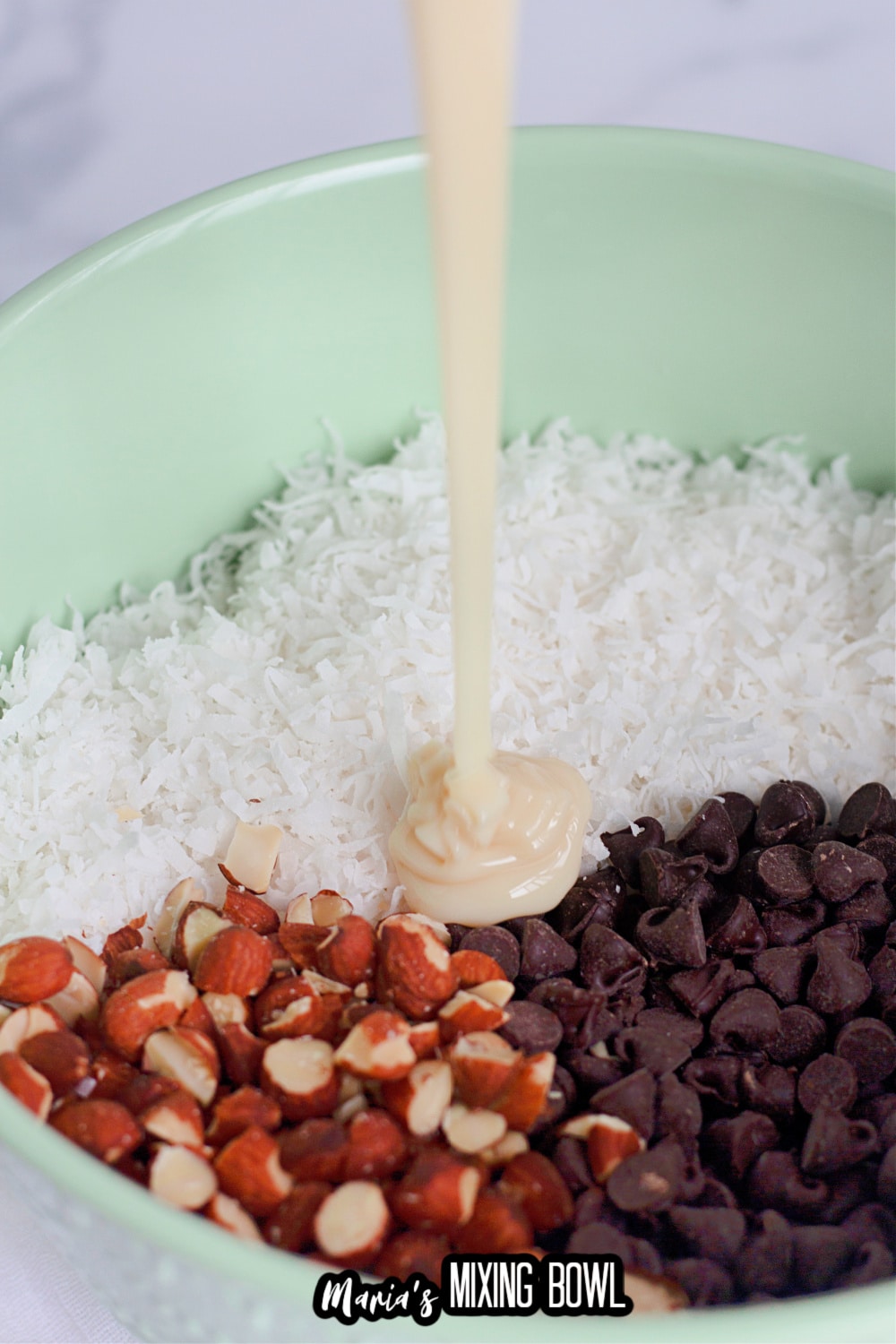 coconut, sweetened condensed milk, almonds, and chocolate chips in a green mixing bowl