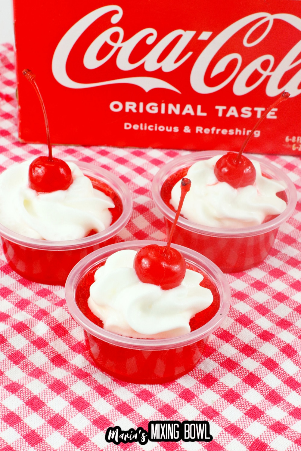 three cherry coke jello shots on a red and white kitchen towel