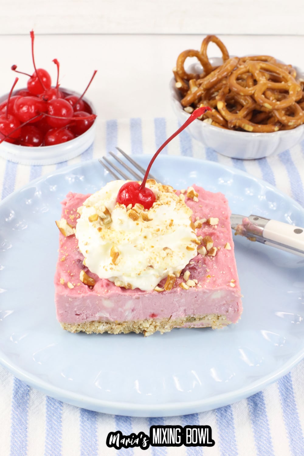 slice of cherry delight on a light blue plate topped with whipped cream and a cherry