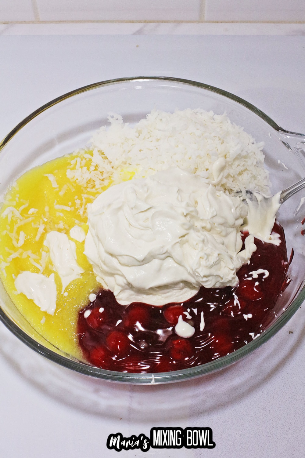 whipped cream, pineapple and cherry pie filling in a glass mixing bowl