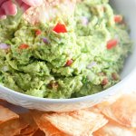 homemade guacamole in a white plate surrounded tortilla chips