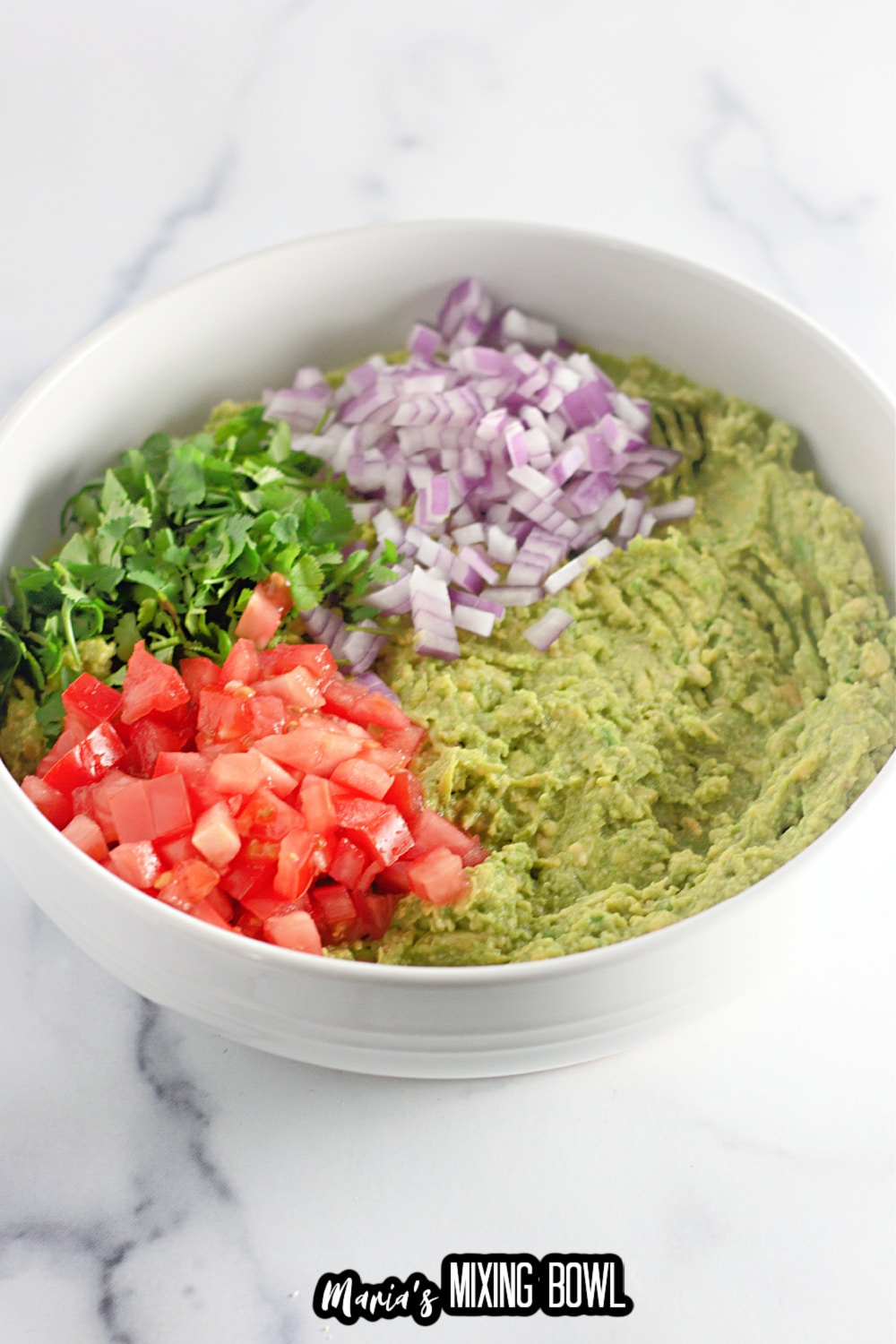 mashed avocado, diced tomatoes, red onions, and cilantro in a large white mixing bowl