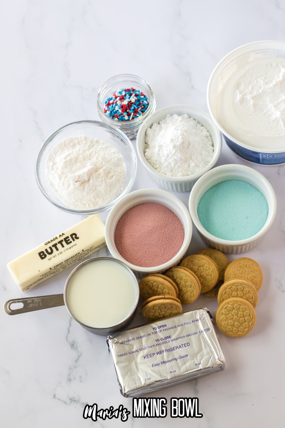 small bowls of sprinkles, cool whip, gelatin powders, cream cheese, heavy cream, stick of butter on a white marble background