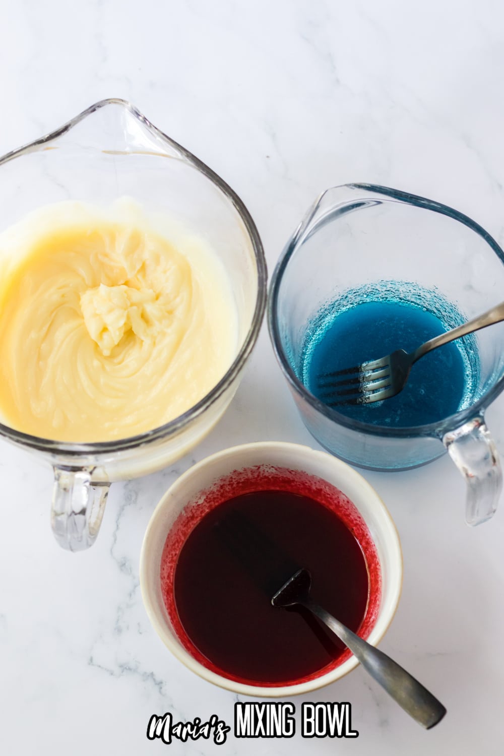 pudding in a small glass mixing bowl, and red and blue gelatin mixed with water in small bowls