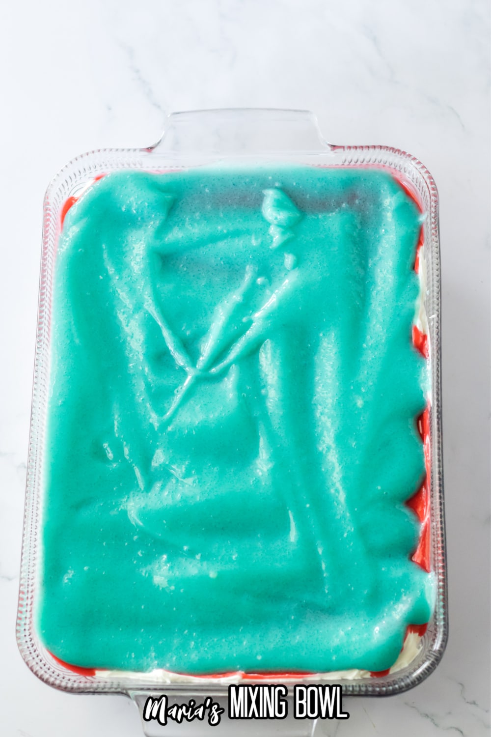 blue pudding being spread on top of the dessert in a glass baking dish