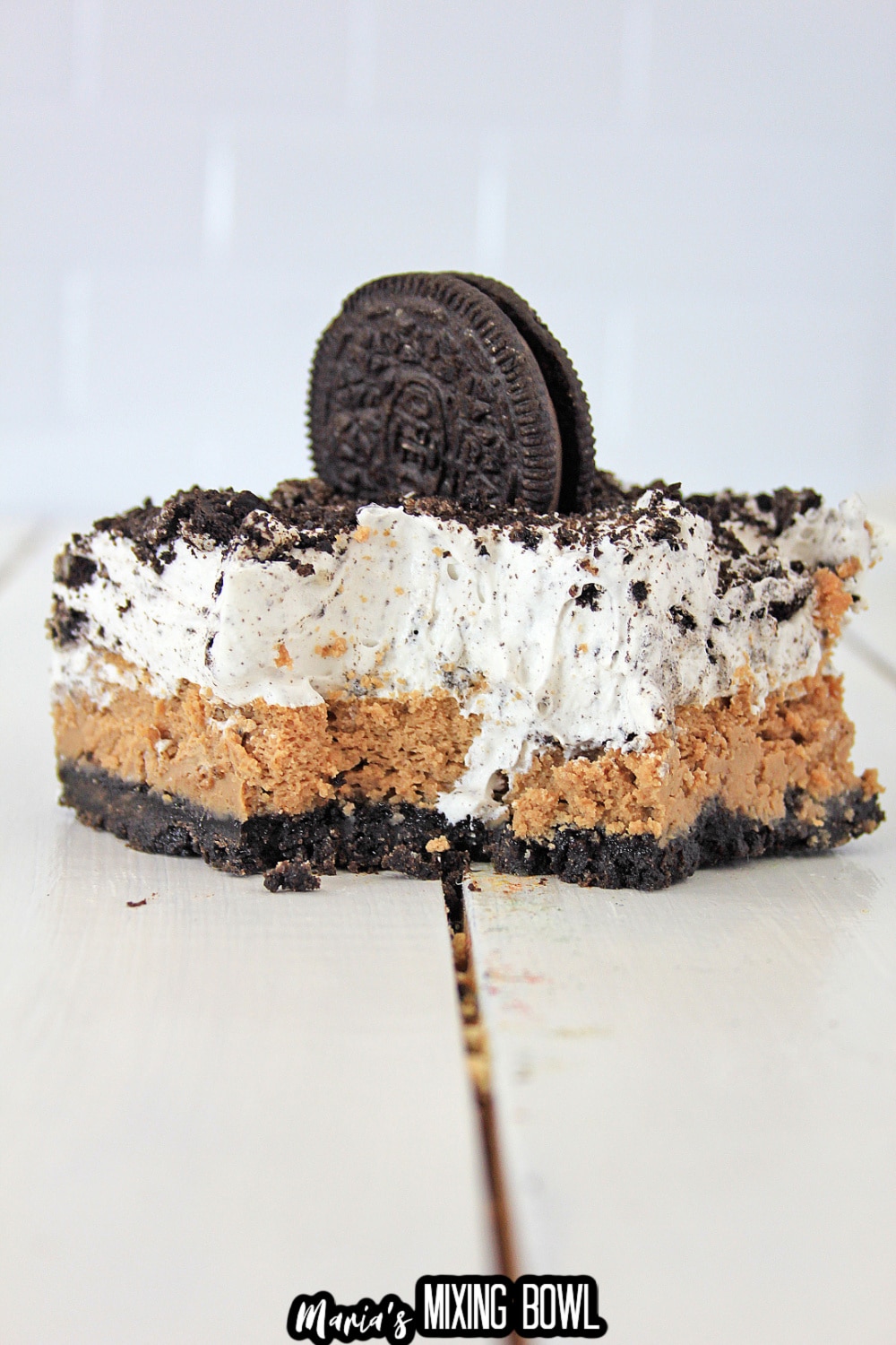 slice of oreo cheesecake delight with a bite missing on a white wooden background