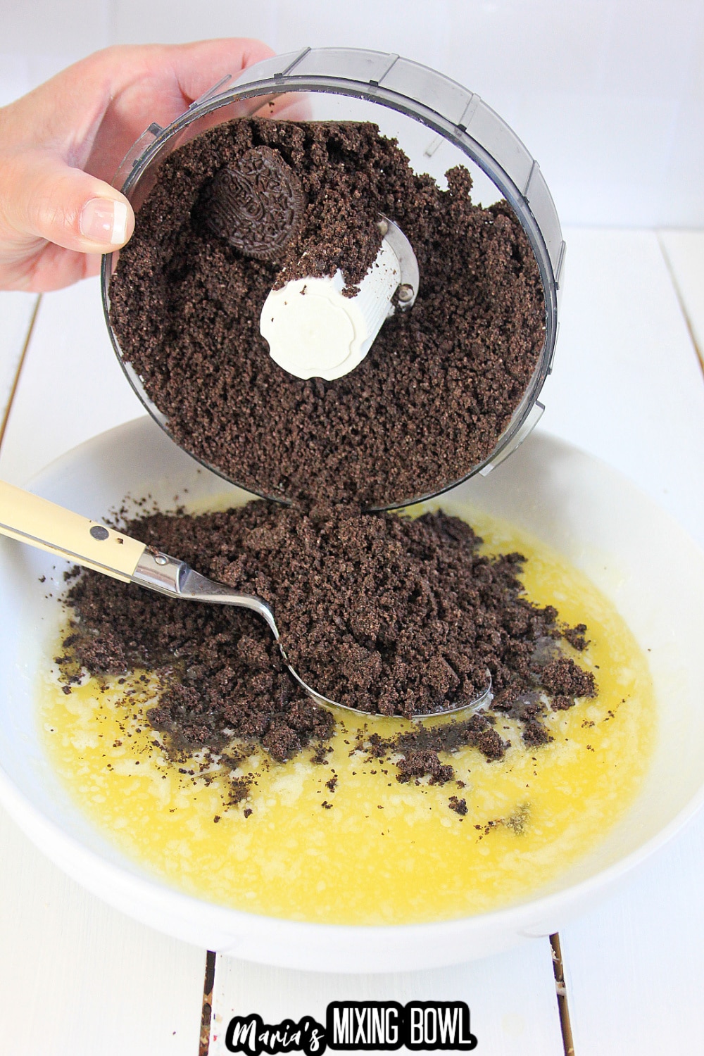oreo cookie crumbs being mixed with melted butter in a small white bowl