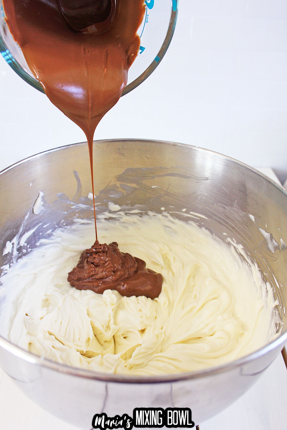 melted chocolate being poured into cheesecake batter in a stand mixing bowl