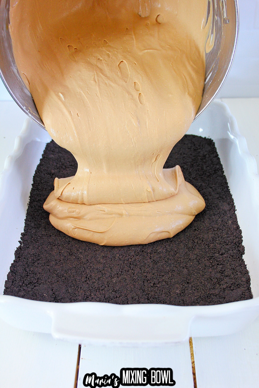 cheesecake batter being poured on top of oreo cookie crust in a parchment lined baking sheet