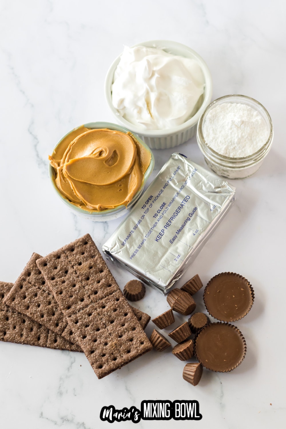 bowls of peanut butter, whipped topping, cream cheese, powdered sugar, chocolate graham crackers, and peanut butter cups