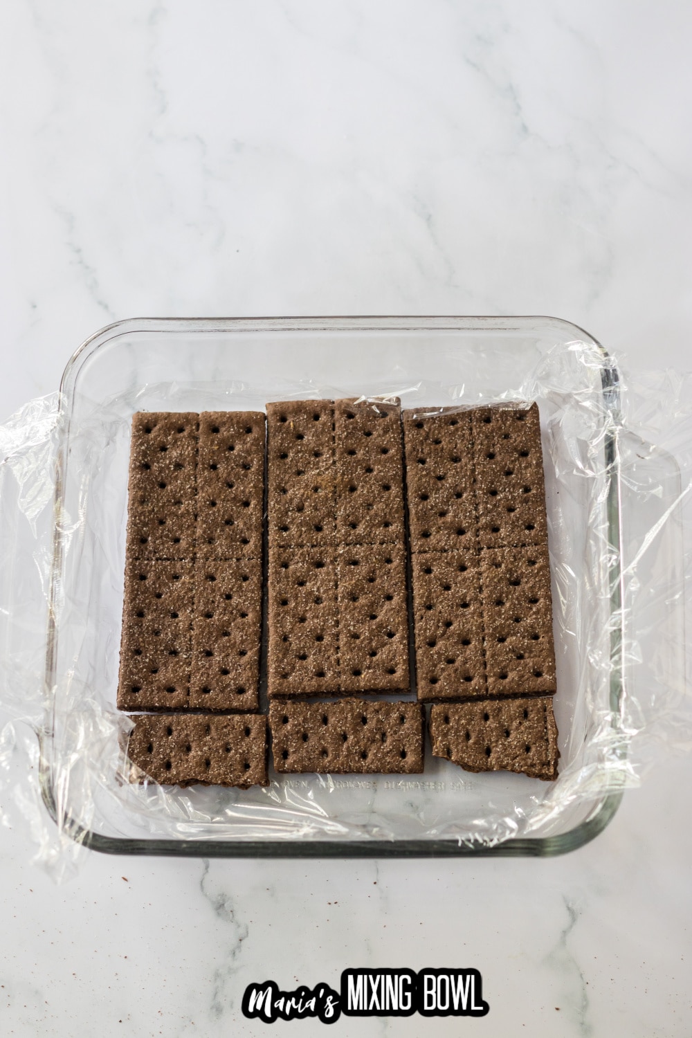 chocolate graham crackers laid on top of plastic wrap in a glass square baking dish