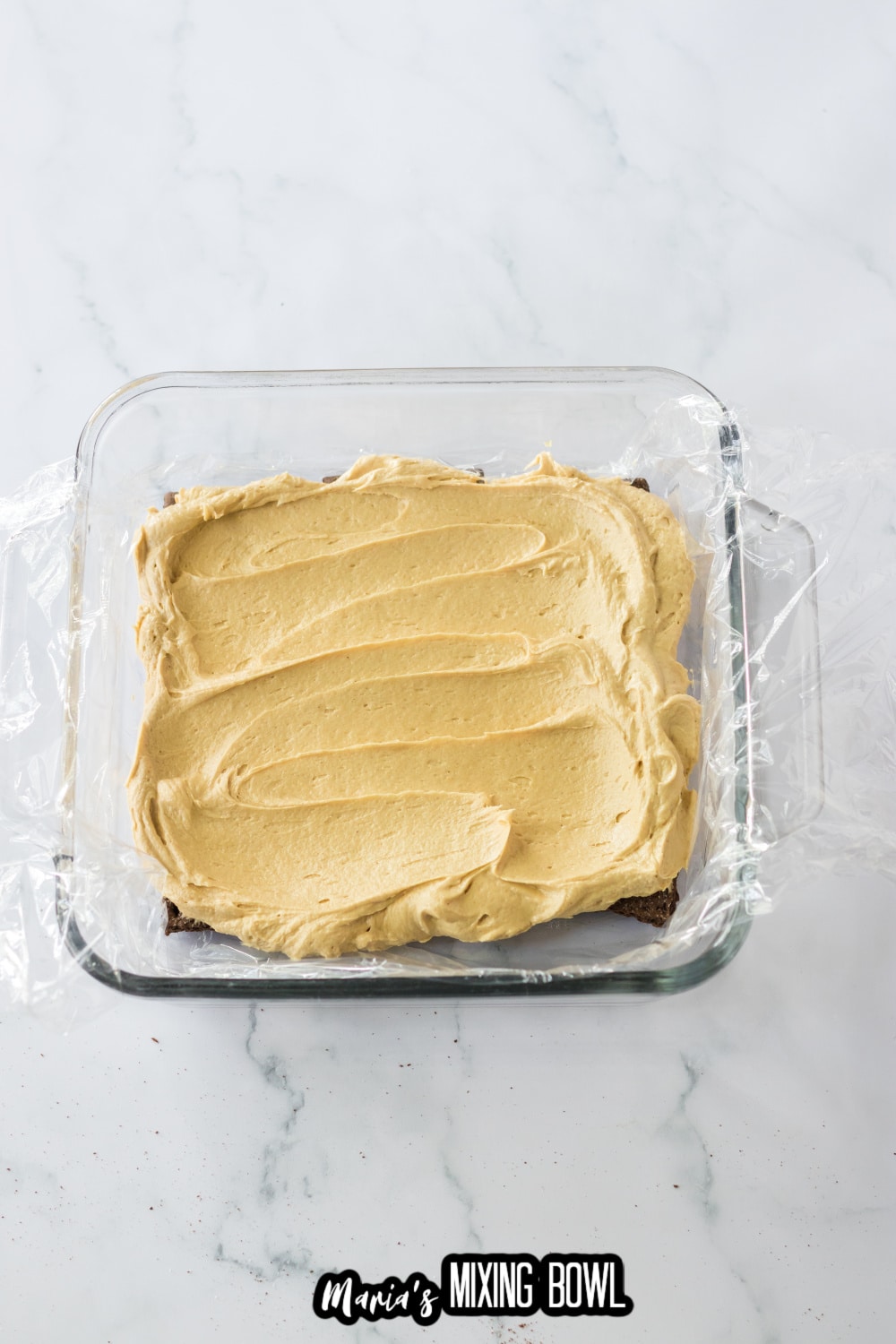 peanut butter cream cheese mixture being spread on top of graham crackers in a glass baking dish