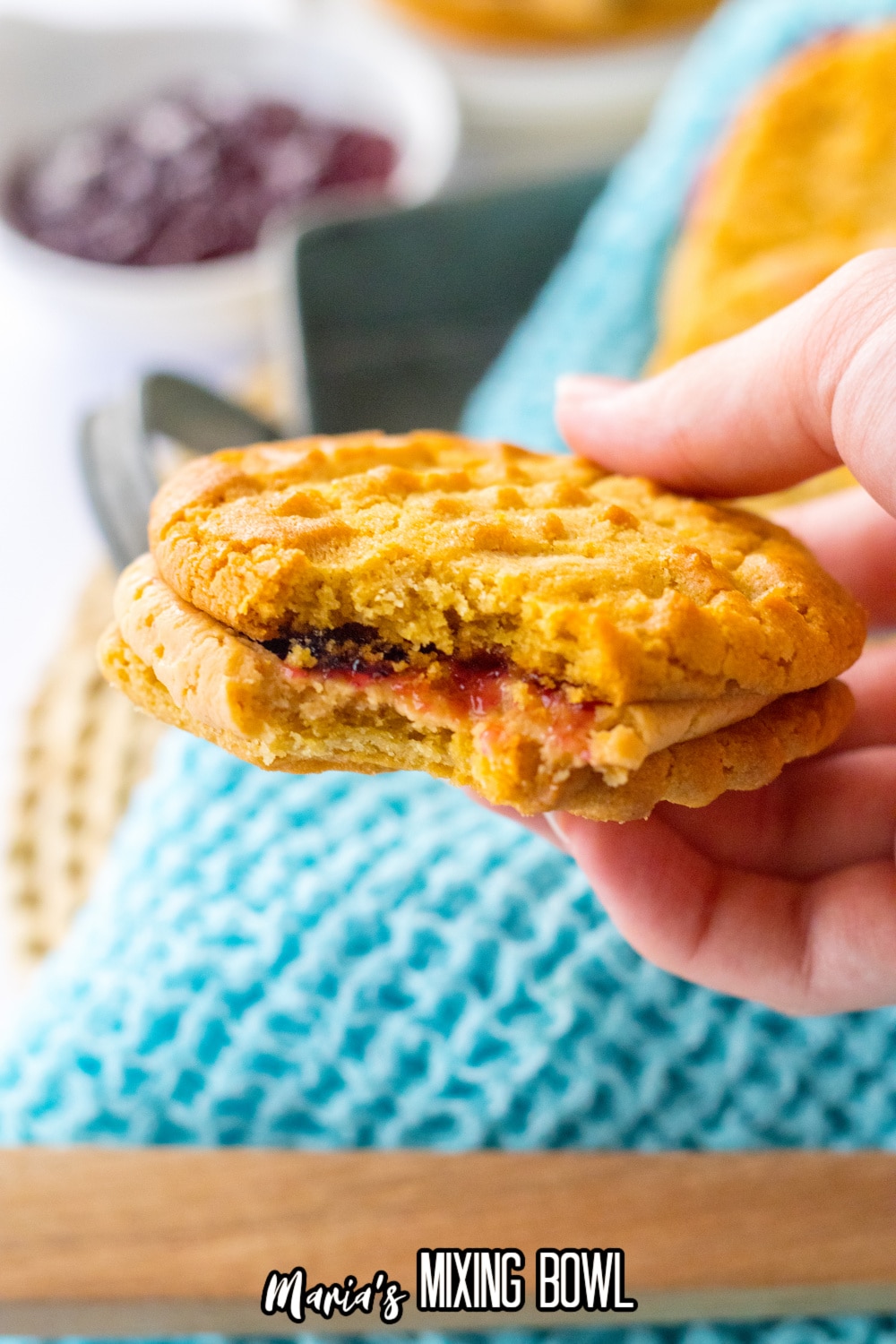 peanut butter and jelly cookie sandwich held in the air in a woman's hand