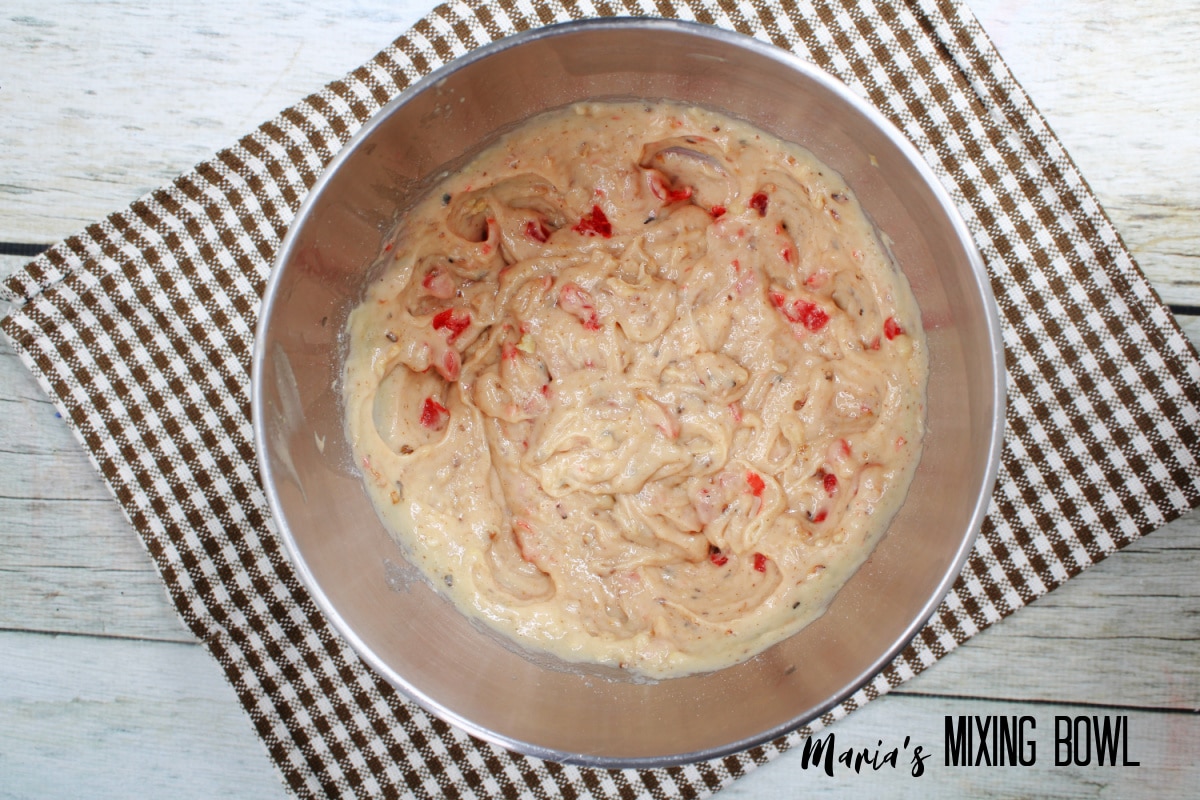 muffin batter in a stainless steel mixing bowl on a brown and white checkered kitchen towel