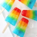 five rainbow popsicles on a white plate