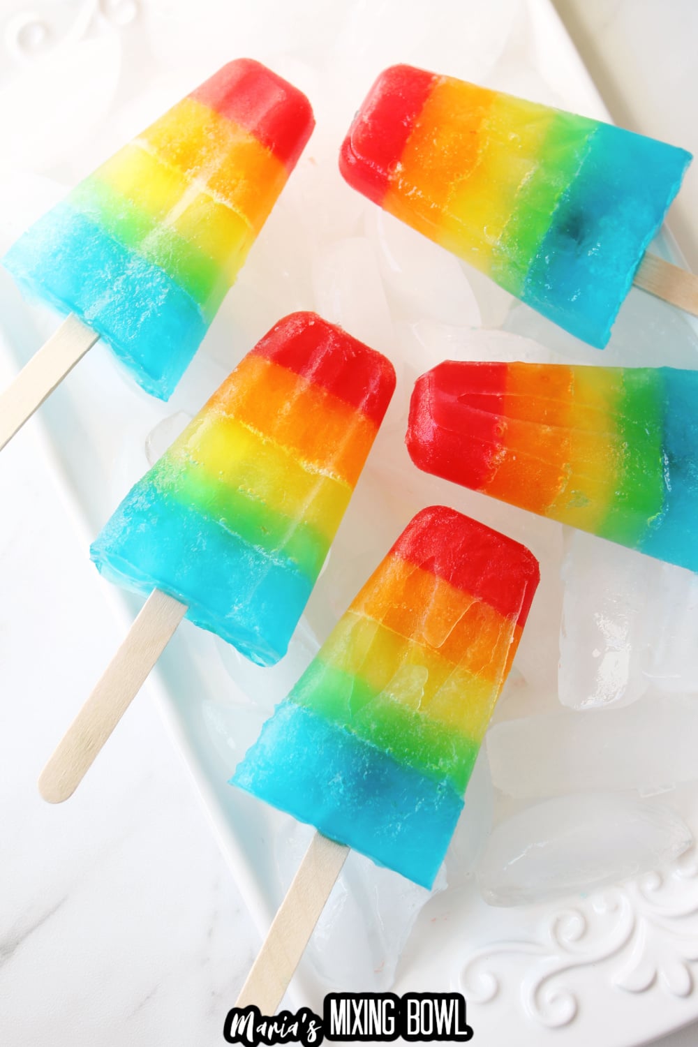 five rainbow popsicles on a white plate