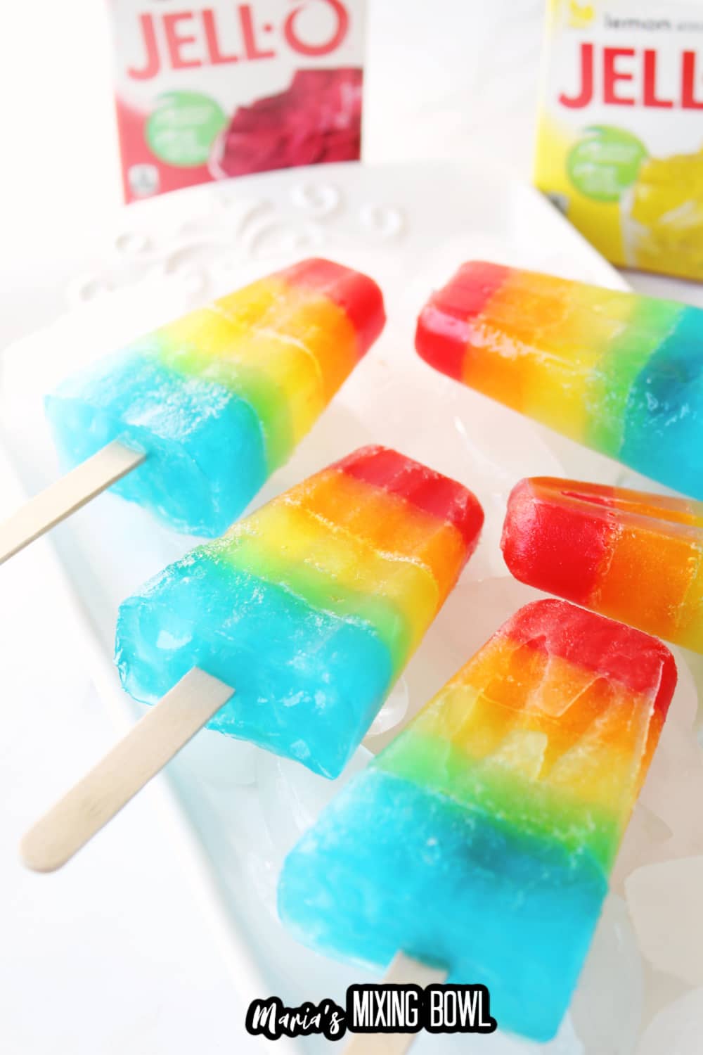 five rainbow popsicles on a white plate