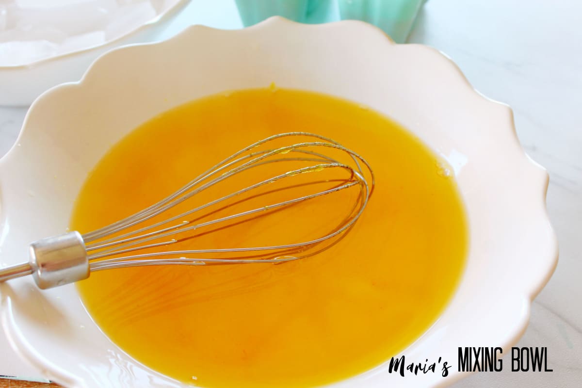 orange gelatin being mixed in a white bowl with a whisk