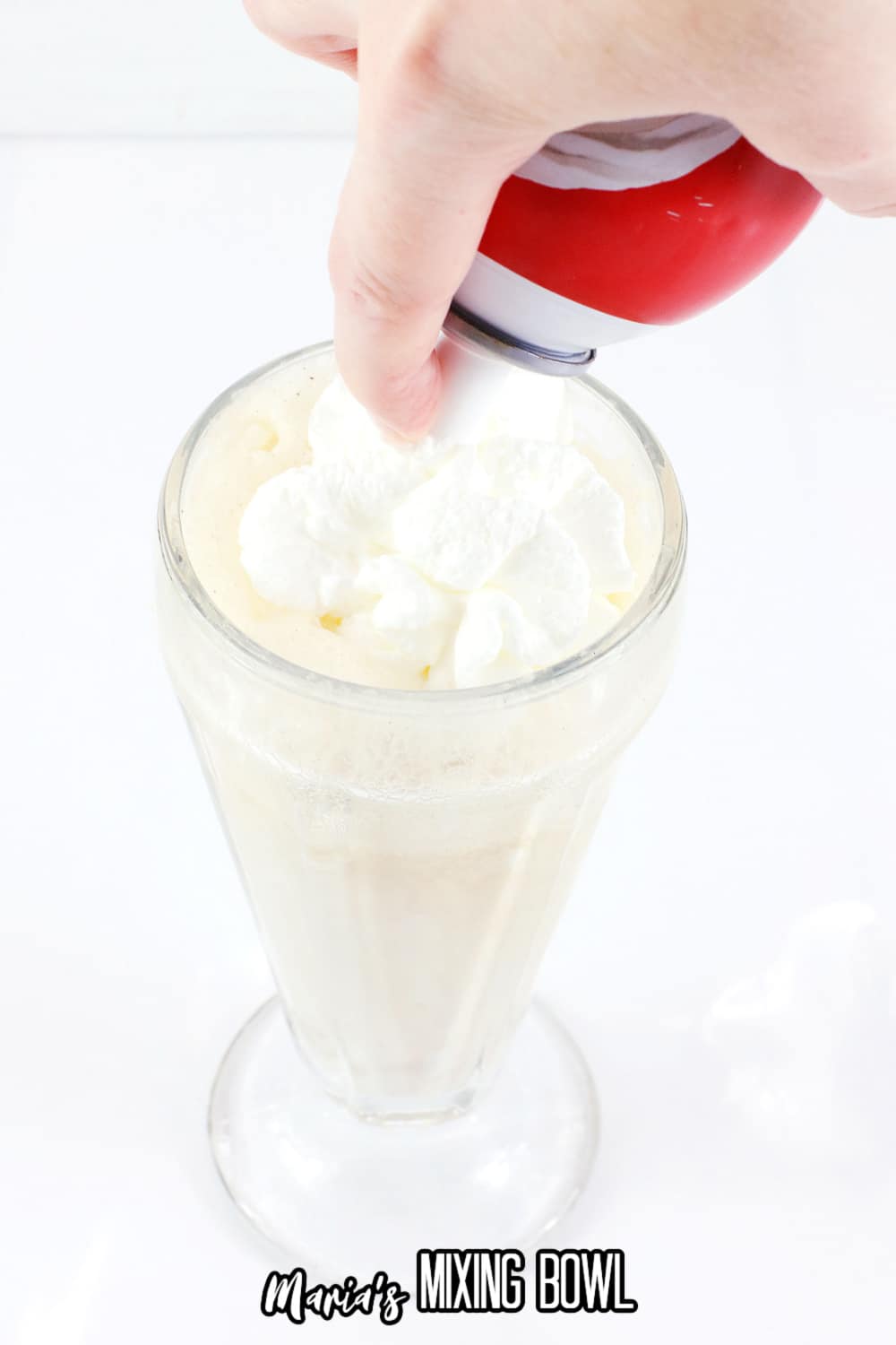 whipped cream being piped on top of a glass filled with root beer