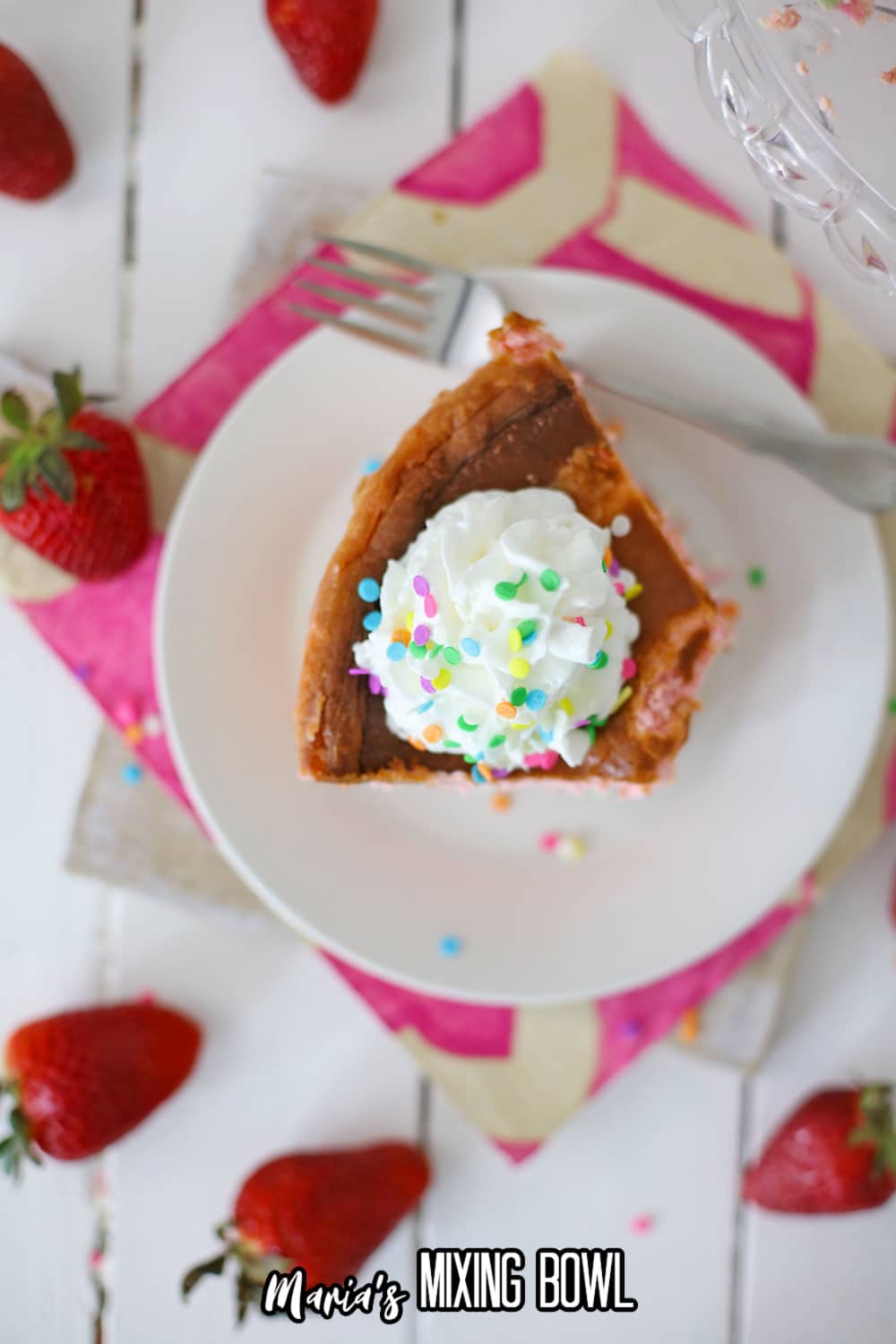 birds eye image of a slice of cheesecake on a small white plate topped with whipped cream