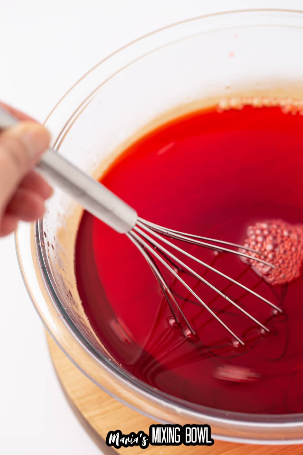 watermelon gelatin being mixed in a large glass bowl with a whisk