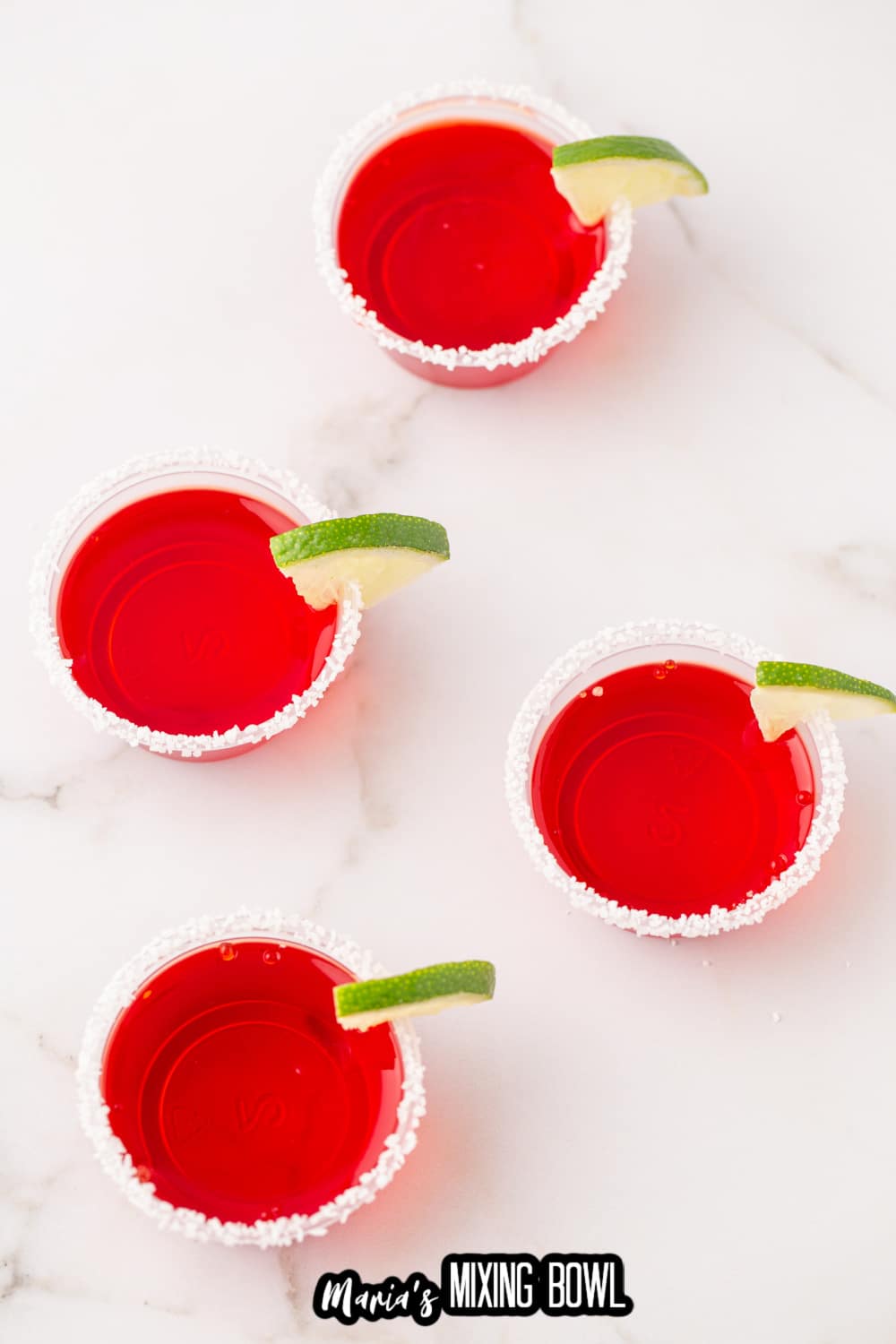 four margarita shots rimmed with salt and a lime wedge