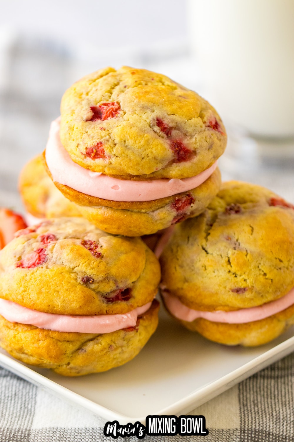 Three strawberry shortcake sandwich cookies on a white plate.