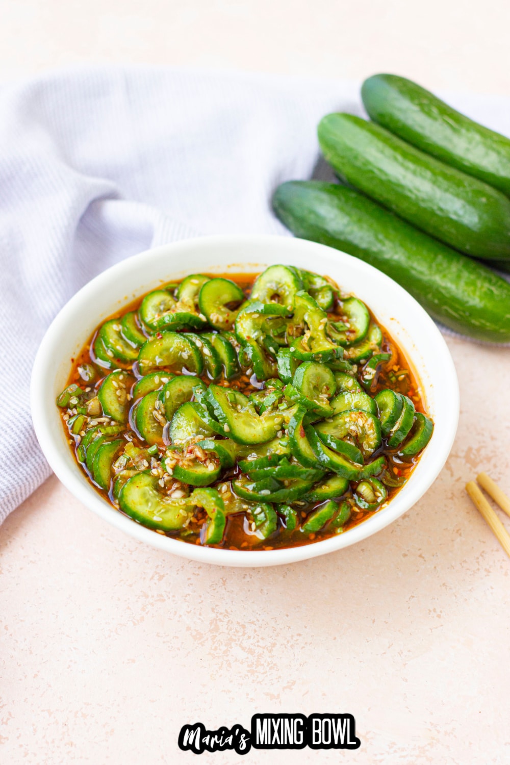 cucumber salad in a white bowl with a stack of cucumbers behind it