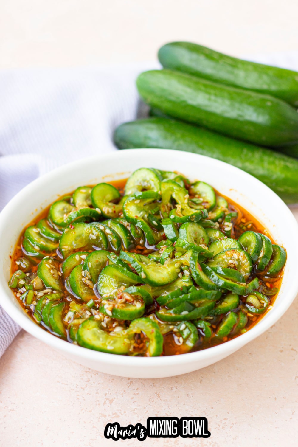 cucumber salad in a white bowl with a stack of cucumbers behind it