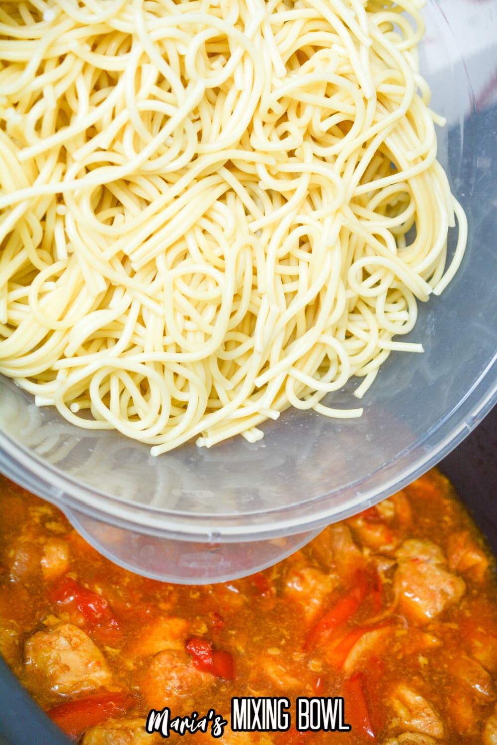 cooked spaghetti noodles being poured into a slow cooker with cooked chicken