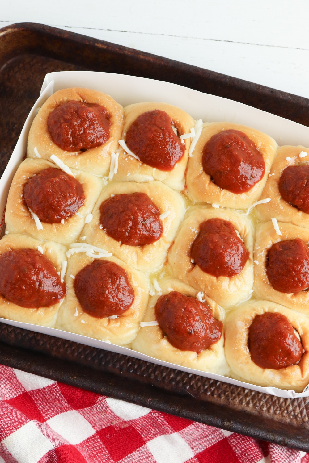 pasta sauce being adding on top of meatballs in rolls on a baking sheet