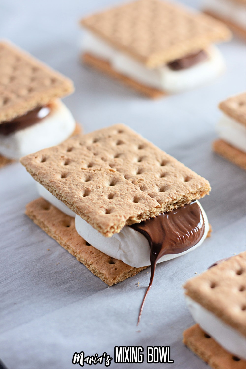 finished smore with melted chocolate coming out the side on a parchment lined baking sheet