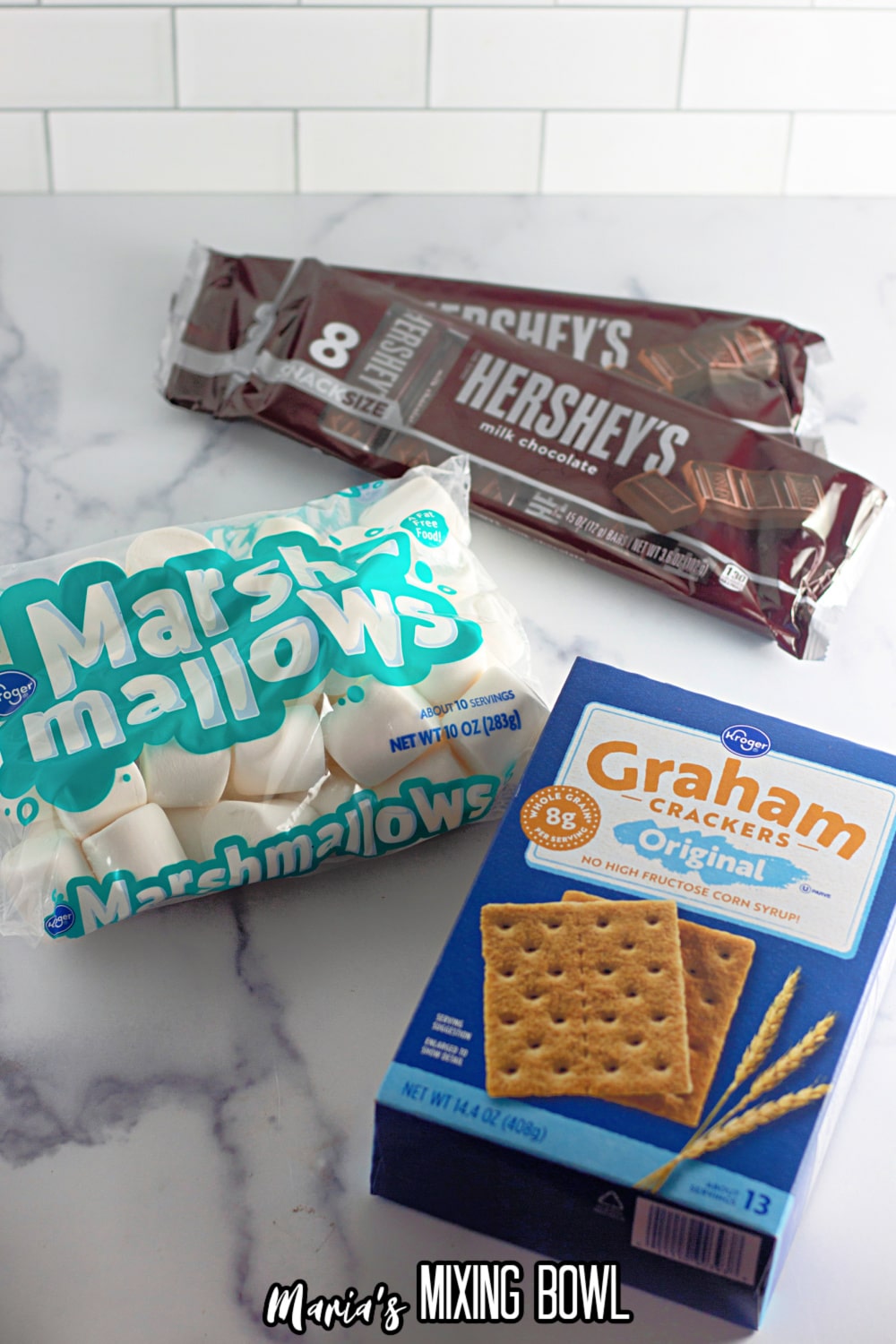 packages of family size Hershey bars, large marshmallows and a box of graham crackers on a marble counter