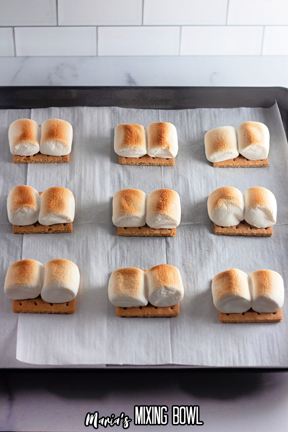 toasted marshmallows on top of graham crackers on a parchment lined baking sheet